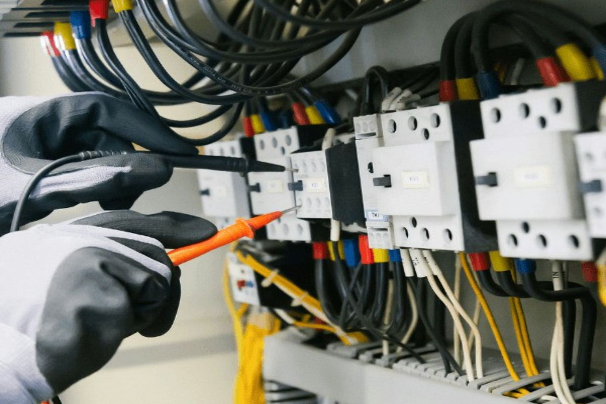 手袋をした手で分電盤の配線を確かめる様子（●●電設株式会社のサンプルサイトより）