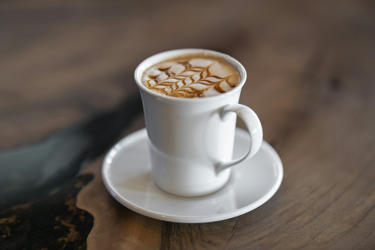 木のテーブルの上の、ラテアートが描かれたカフェラテ(Unsplashの写真)